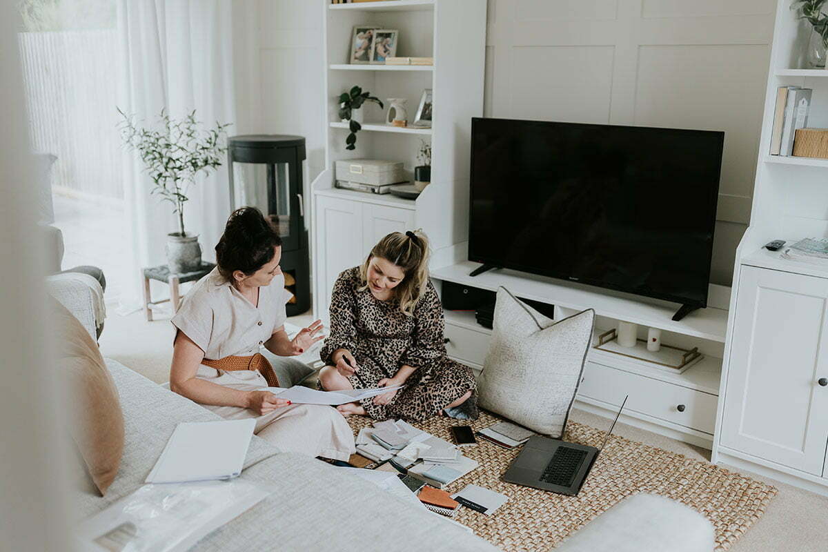 Danielle and Emily sitting on rug with various notepads and fabric swatches with laptop in front | Interior Design Consultation